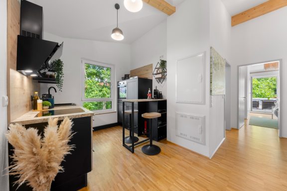 Moderne Küche mit Holzdetails, Barstuhl und großen Fenstern zum Außenbereich.