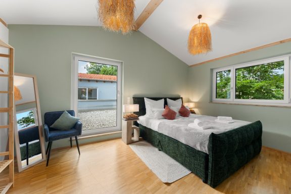 Helles Schlafzimmer mit einem grünen Bett, Fenster und Holzdetails.